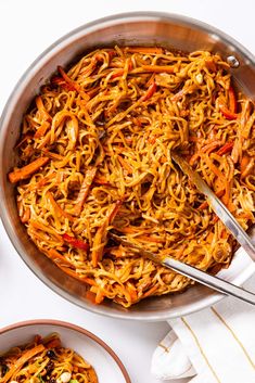 a pan filled with noodles and carrots on top of a white table next to two plates