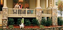 two people are standing on the front porch of a house with a dog walking by