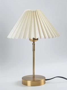 a white lamp with a gold base and a black cord plugged in to it