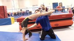 two people doing gymnastics on blue mats in an indoor area with other people looking on