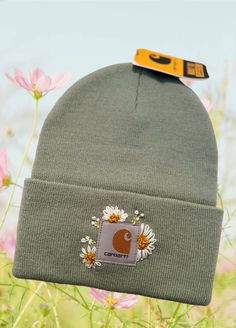 a beanie hat with a patch on the side and flowers in the front, against a background of wildflowers