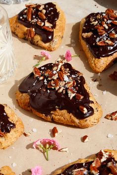 several cookies with chocolate frosting and pecans scattered around them on a piece of parchment paper