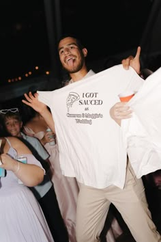 a man holding up a white t - shirt while standing next to other people at a party