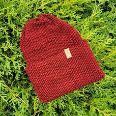 a red knitted beanie laying on top of green grass with a tag in the middle