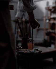 a person holding a paintbrush in front of a cup filled with brushes on top of a table