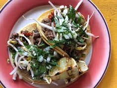 two tacos on a plate with onions, meat and cilantro sprouts