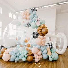 a bunch of balloons floating in the air on top of a wooden floor next to a wall