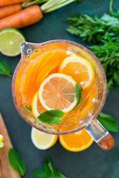 a pitcher filled with orange juice surrounded by carrots and herbs