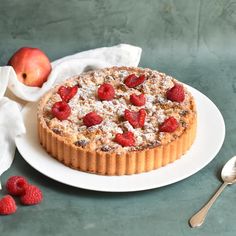 a dessert on a white plate with raspberries and an apple in the background