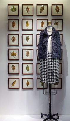 a mannequin is dressed up in a dress and jacket with leaves on the wall behind it