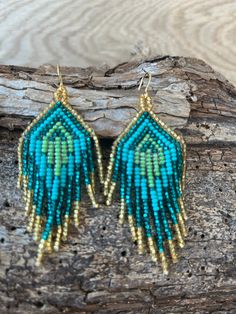 a pair of blue and green beaded earrings on top of a piece of wood