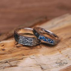 two wedding rings sitting on top of a piece of wood with blue stones in them