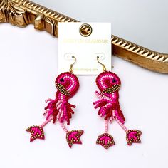 These earrings include multiple color pink beads and a gold detailing. Hanging from the bottom of the flamingo shaped beaded pendant has dangling legs. These earrings are pictured leaning agasint a gold mirror on a white background. Bohemian Jewelry For Summer Beach Party, Trendy Beaded Jewelry For Beach Season, Multicolor Summer Jewelry, Casual Summer Party Earrings, Beaded Trendy Jewelry For Beach Season, Bohemian Jewelry For Beach Season Parties, Bohemian Beach Season Party Jewelry, Bohemian Beaded Earrings For Vacation, Trendy Multicolor Beaded Earrings For Summer