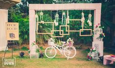 a white bike parked under a wooden structure next to a lush green forest filled with flowers