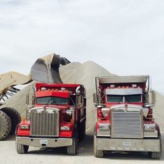 two large trucks parked next to each other in front of a pile of dirt and machinery