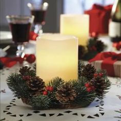 two lit candles sitting on top of a table covered in pine cones and holly wreaths