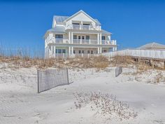 a house on the beach with a fence in front of it and sand behind it