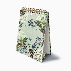 a spiral notebook with flowers and birds printed on it, sitting upright against a white background