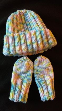 two knitted hats and mittens sitting next to each other on a black surface