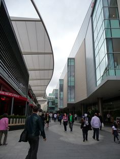 many people are walking down the sidewalk in front of some tall buildings with glass windows