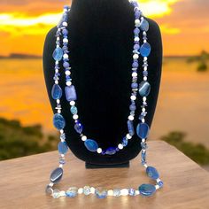 This stunning necklace measures 35 inches and features blue lapis lazuli, complemented with pearls, crystals, and iridescent stones. According to the Sumerians, the lapis lazuli stone housed the spirit of their gods, while the ancient Egyptians regarded it as a representation of the night sky. Lapis lazuli has always been connected to qualities such as strength, courage, intelligence, truth, royalty, and wisdom since ancient times. This necklace can brighten up any room with its bedazzling sparkle. Wrap it three times with the lighter-colored stones at the bottom. Blue Kyanite Jewelry With Gemstone Beads, Blue Kyanite Gemstone Beads Jewelry, Blue Long Hand-strung Necklace, Blue Gemstone Beads Necklace, Bohemian Blue Pearl Necklace With Gemstone Beads, Blue Hand-strung Long Necklace, Blue Bohemian Pearl Necklace With Gemstone Beads, Spiritual Sodalite Beaded Jewelry, Artisan Blue Gemstone Crystal Necklace