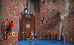 several people climbing up and down the side of a wall in an indoor climbing gym