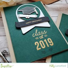 a green graduation card with the words class of 2019 written in gold on it next to some scissors and flowers