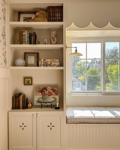 a white book shelf with books and other items on it in front of a window