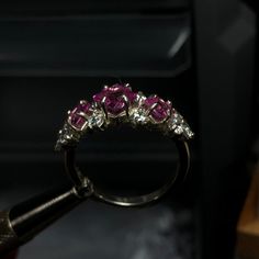 A beautiful cluster ring, set with three princess cut gemstones surrounded by ten round cut accents. This ornate ring is crafted with elegancy and designed to draw the eyes in. Pictured is three princess cut Pink Sapphires and accented with cubic zirconia. A plethora of stones are available for selection and the ring can be customized/mixed and matched with up to 13 different gemstones on one ring! Disclaimer: she tends to tarnish easy in between the gems, so a good chemical cleaner or toothbrus Princess Cut Jewelry With Accent Stones, Princess Cut Diamond Ring With Accent Stones For Promise, Exquisite Pink Sapphire Ring, Dazzling Cluster Promise Ring Jewelry, Luxury Pink Sapphire Ruby Ring, Exquisite Pink Sapphire Gemstone Rings, 14k White Gold Jewelry With Princess Cut Prong Setting, Dazzling Diamond Cluster Ring With Accent Stones, Diamond White Princess Cut Jewelry With Accent Stones