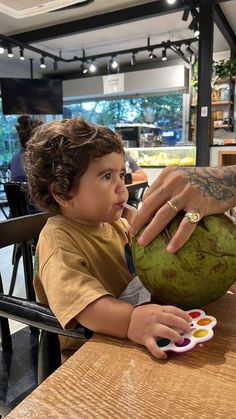 a little boy sitting at a table with a green coconut