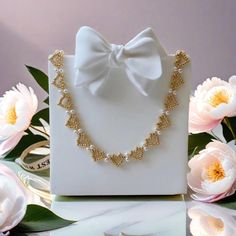 a white box with a necklace on it next to some flowers and pink peonies