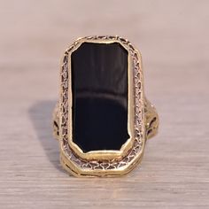 This Stunning Piece, Known As The Art Deco Elegance, Features A Captivating Elongated Emerald Cut Onyx Tablet At Its Center. The Rectangular Cut Onyx Is Elegantly Bezel Set In 14 Karat Yellow Gold, Designed With Intricate Filigree Detailing That Adds A Touch Of Vintage Sophistication Which Continues Down The Shank. The Ring Is Crafted In 14 Karat Yellow Gold And Is Currently A Finger Size 2.75 But Can Be Adjusted To Any Finger Size For An Additional Charge Upon Request, Ensuring A Perfect Fit. Black Heirloom Jewelry For Ceremonial Occasions, Black Heirloom Jewelry For Ceremonial Use, Black Heirloom Ceremonial Jewelry, Luxury Black Filigree Jewelry, Black Heirloom Filigree Jewelry, Heirloom Black Filigree Jewelry, Antique Black Jewelry For Ceremonial Occasions, Ceremonial Black Jewelry With Intricate Design, Antique Black Ceremonial Jewelry