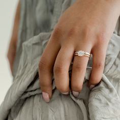 a woman's hand with a diamond ring on her finger, wearing a gray dress