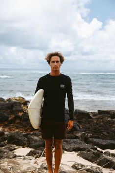 a man holding a surfboard on top of a sandy beach next to the ocean