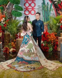 a man and woman standing in front of a display with flowers on the wall behind them