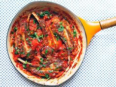 a skillet filled with meat and sauce on top of a blue tablecloth next to a wooden spoon