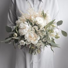 a man holding a bouquet of white flowers and greenery in his hands, against a gray background