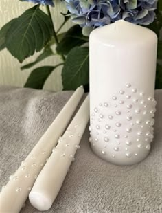 two white candles sitting next to each other on a table with blue flowers in the background