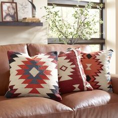 a brown leather couch with pillows on top of it in front of a window filled with pictures