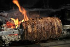 a large piece of meat is being cooked over an open fire