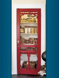 a red china cabinet sitting inside of a kitchen next to a wall with shelves filled with jars and containers