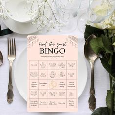 a place setting for a wedding with flowers and silverware on the table, along with a pink sign that says find the guest bingo