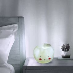 an apple shaped lamp sitting on top of a night stand next to a white bed