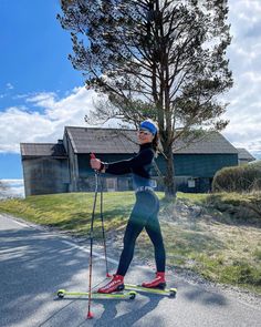 a woman riding skis on top of a road next to a tree and grass covered field