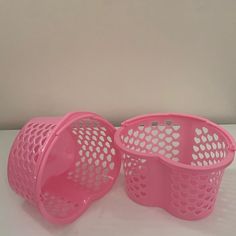 two pink plastic baskets sitting next to each other on a white counter top in front of a wall