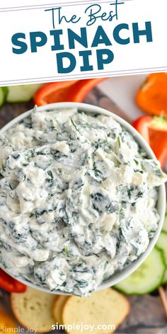 spinach dip in a bowl with sliced cucumbers and carrots on the side