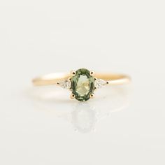 an oval green and white diamond ring with three small diamonds on the band, set in yellow gold