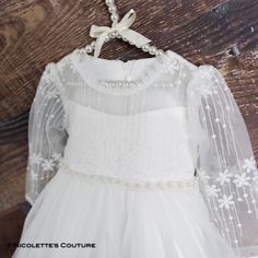 "This dress is just beautiful! It is white with a soft underlining and a lace detail on top. Finished with tulle and a lace bottom to add that extra cute factor! The sheer long sleeves are perfect for all seasons. Perfect for your next special event. Nicolette's Couture is a family owned boutique based out of Dubuque, Iowa. When creating looks, comfort is our main priority...regardless of how chic a style is. Our popular special occasion styles are trendy, but won't make your girl itch. (Complai White Ruffled Baptism Dress, White Lace Baptism Dress With Floral Applique, White Baptism Dress With Ruffles For Dress-up, Elegant Off-white Lace Baptism Dress, White Tulle Baptism Dress With Bow, Baby Baptism Dress, Tulle Wedding Gown, Baptism Gown, Heirloom Dresses