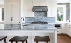 a large kitchen with white cabinets and marble counter tops, along with bar stools