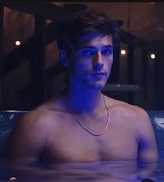 a shirtless man sitting in a hot tub looking at the camera with blue light on his face